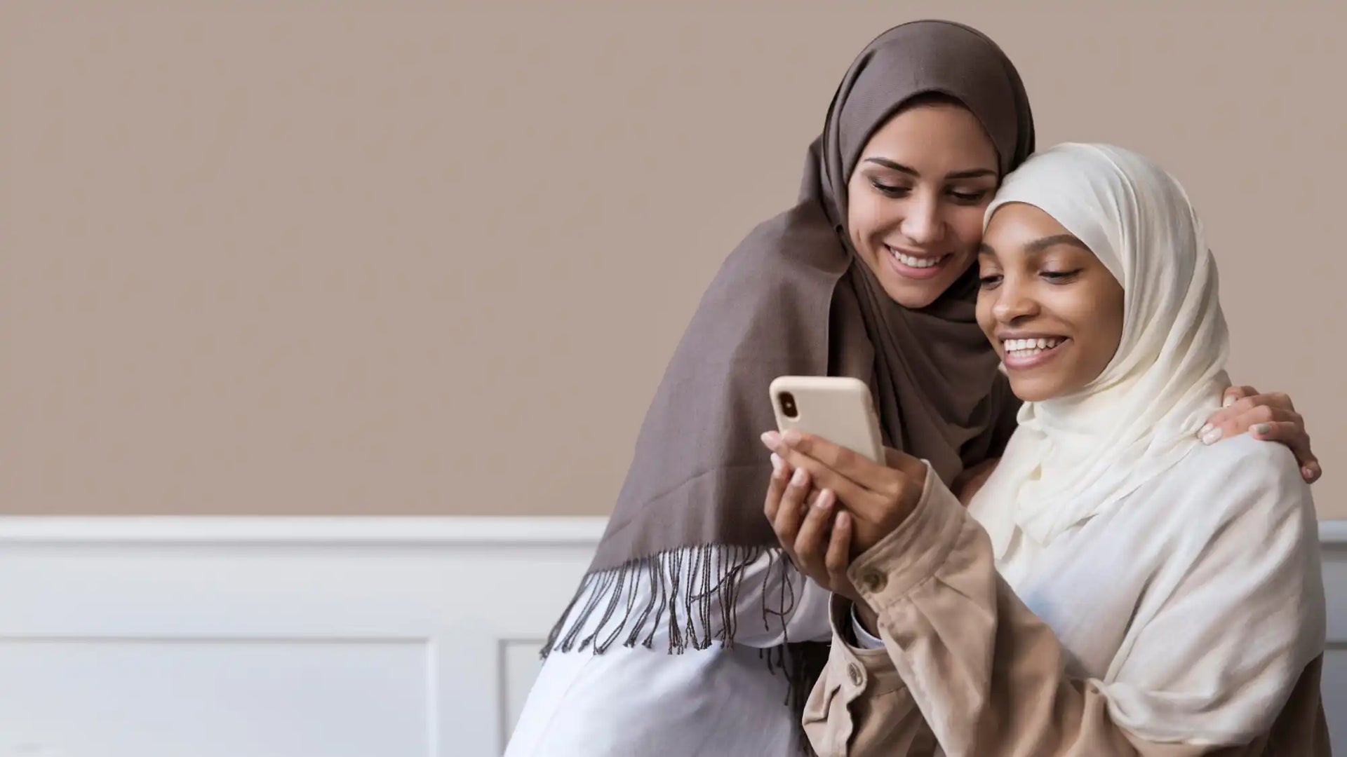 Two women in hijabs looking at a phone.