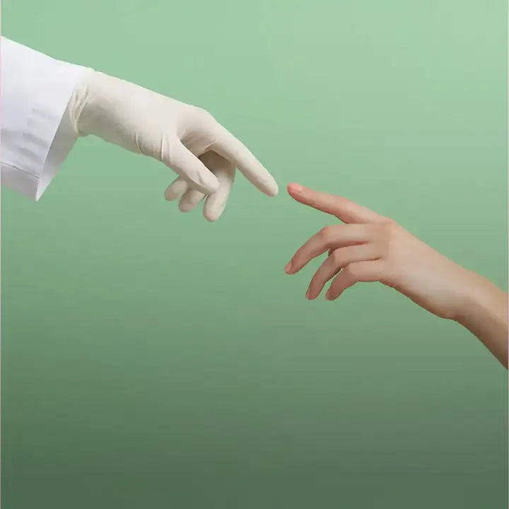 A white latex medical glove on a gloved hand reaching toward an ungloved finger.