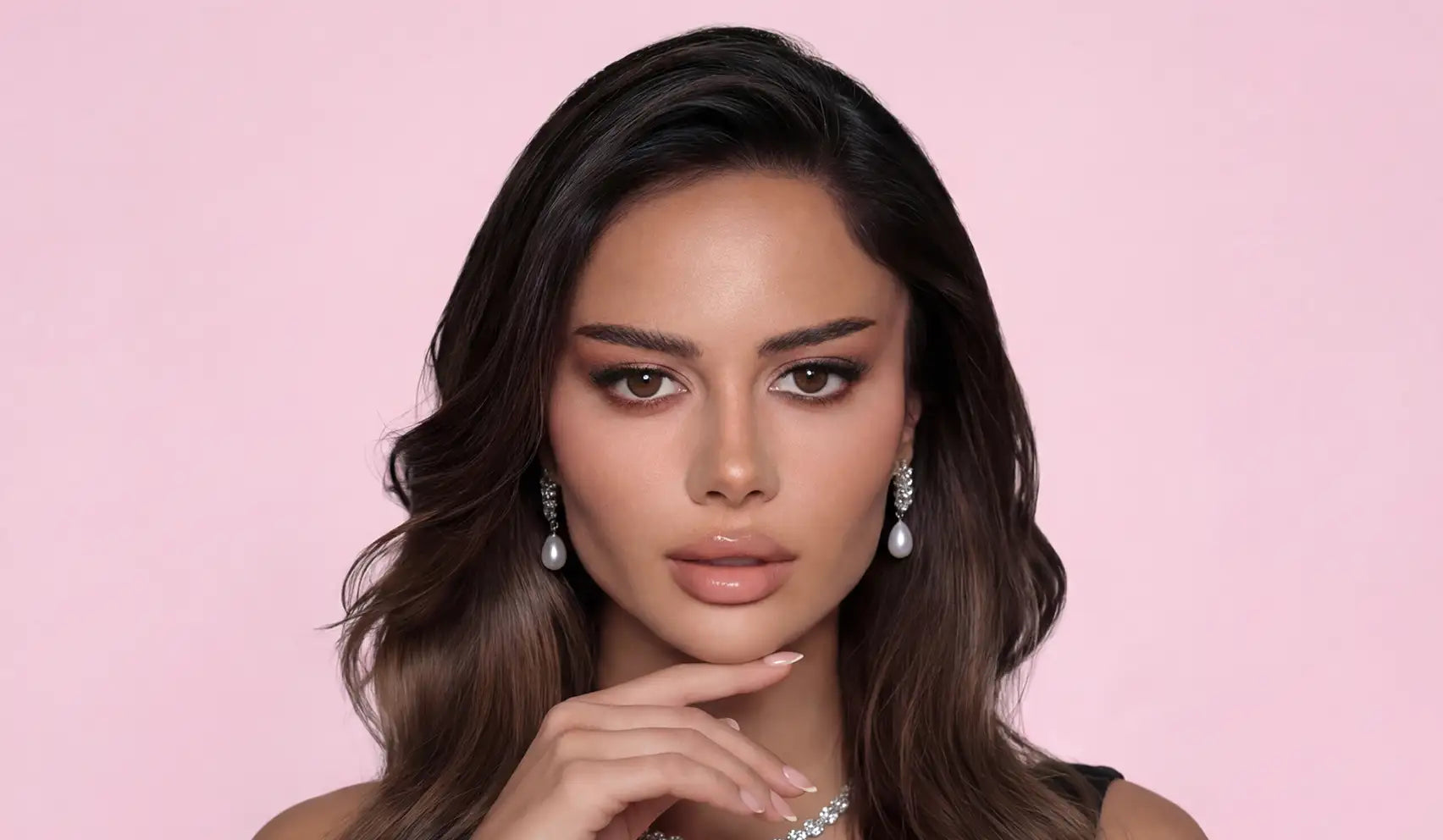 A woman with long, dark brown wavy hair wearing elegant pearl drop earrings and a sparkling diamond necklace.