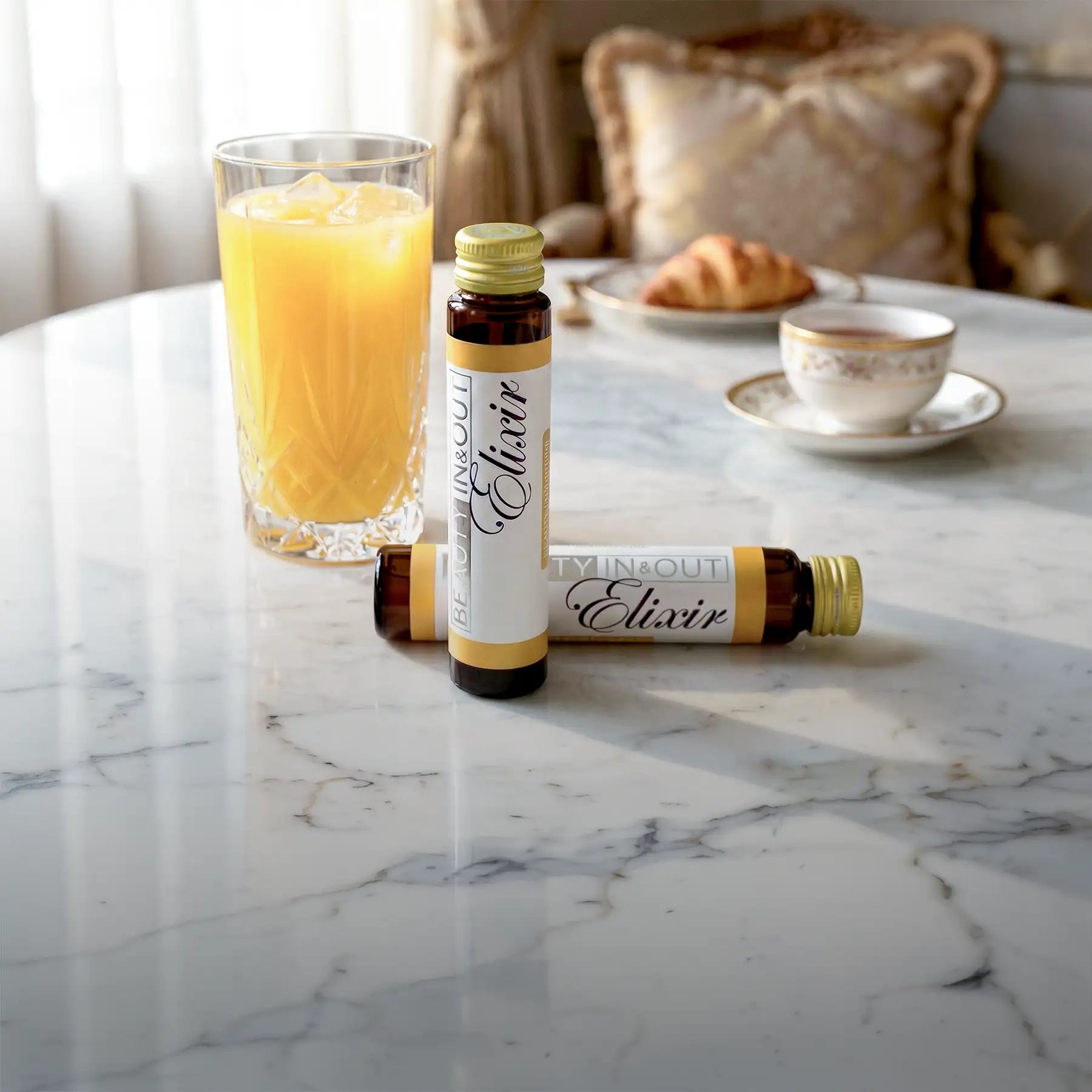 Two amber glass bottles with gold caps and white labels featuring the word ’elixir’ in elegant script, one standing upright and another lying on its side.