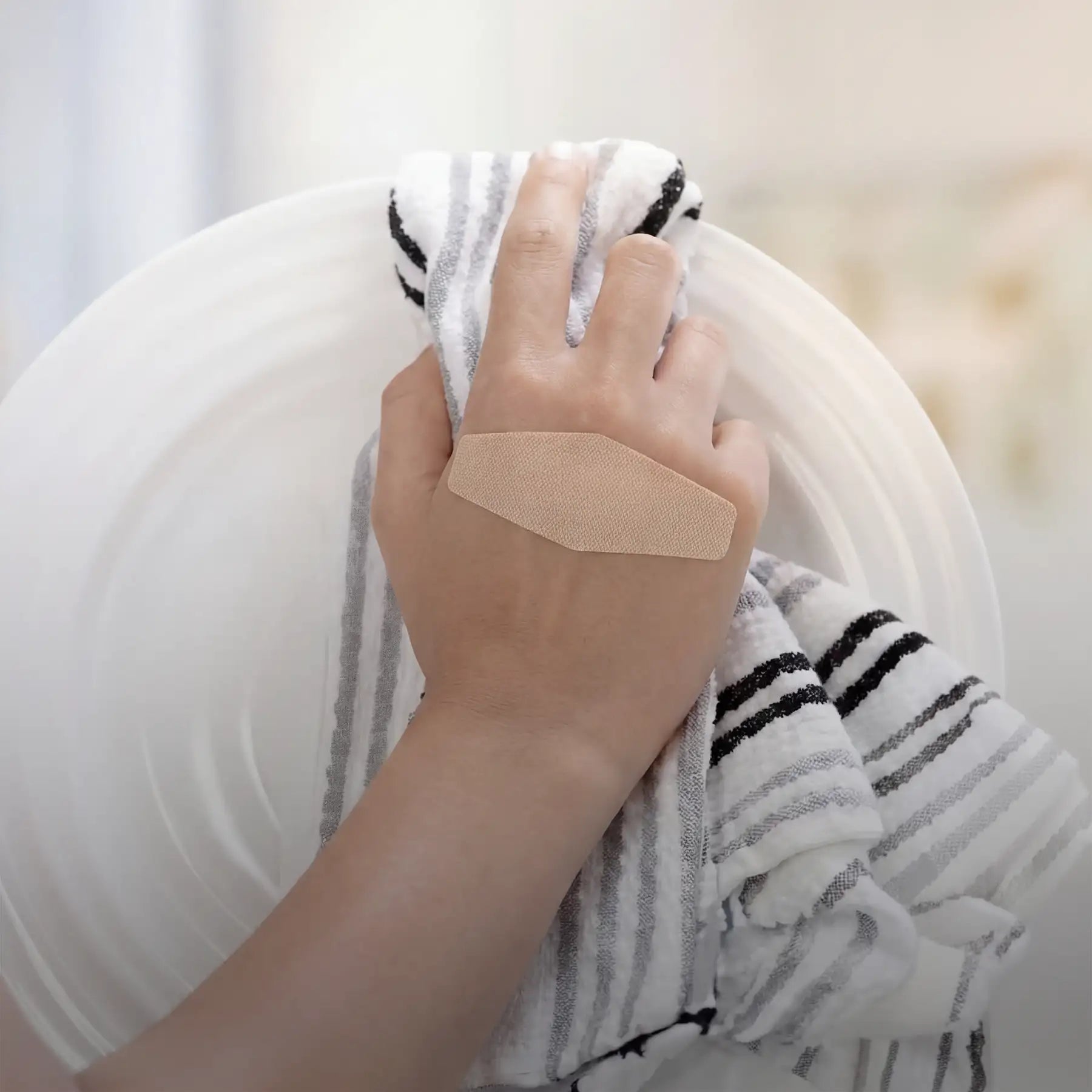 A beige, textured adhesive bandage with a slightly raised edge is applied to the back of a hand.