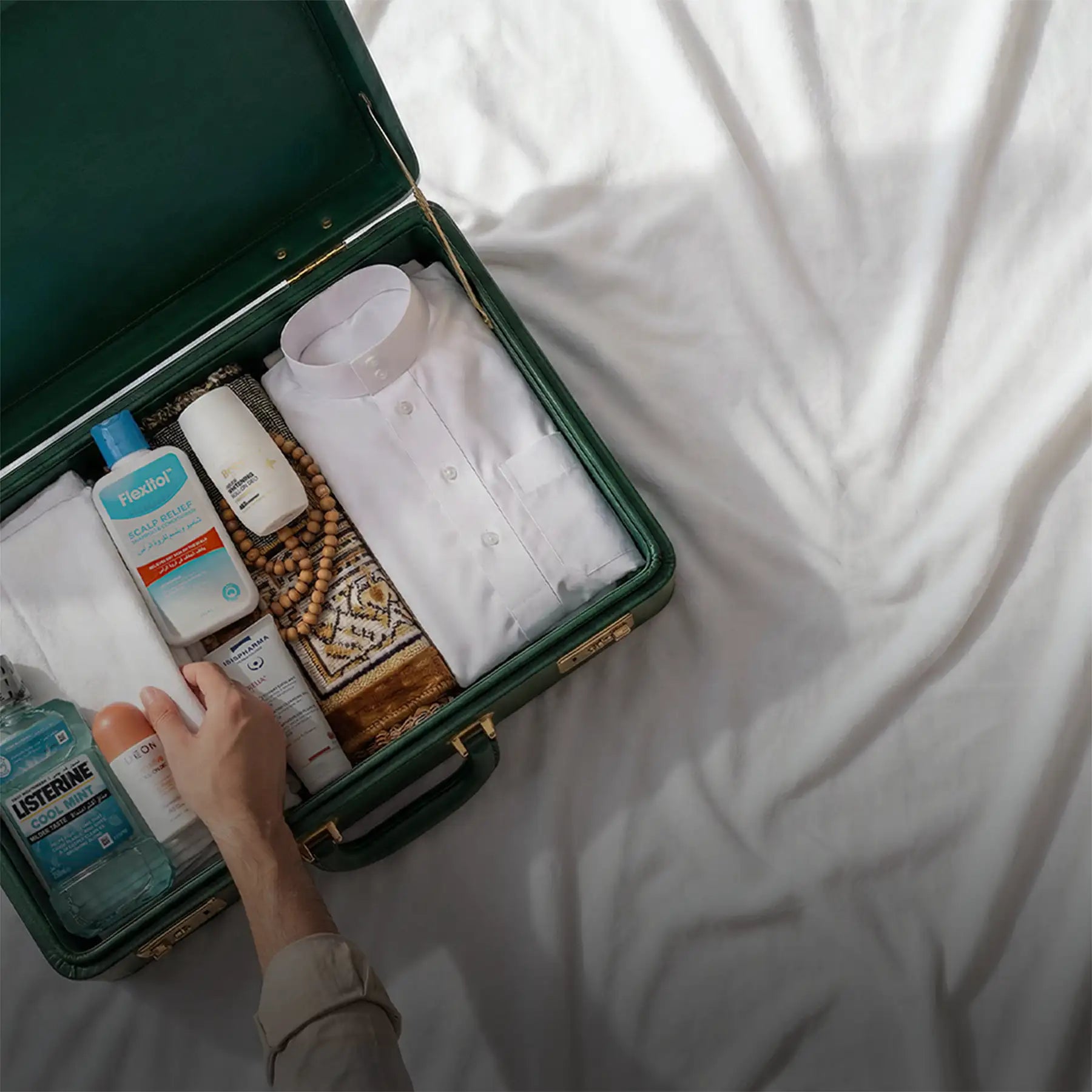 Dark green vintage suitcase with gold-toned hardware and a handle, containing neatly packed travel essentials.