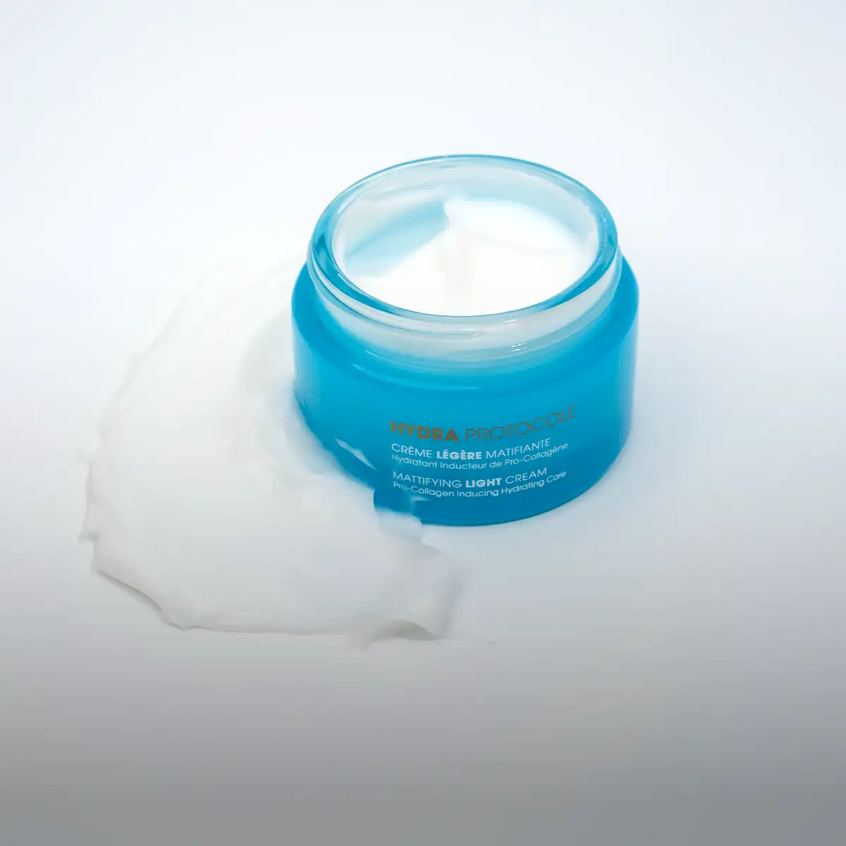 A translucent blue glass jar containing a white, creamy substance with the label ’hydra protection matifying light cream’ visible on its side.