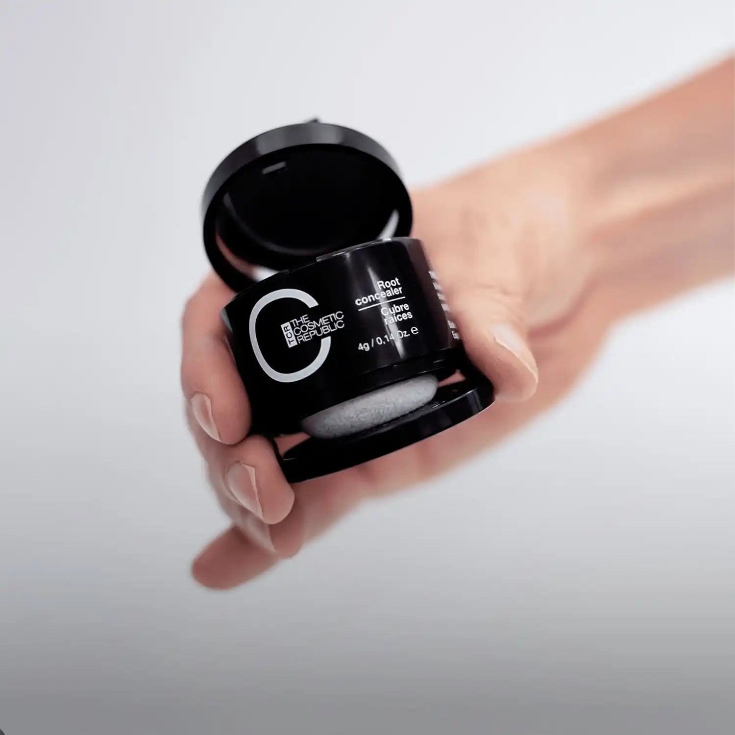 A black container of hair root concealer with a built-in applicator sponge.