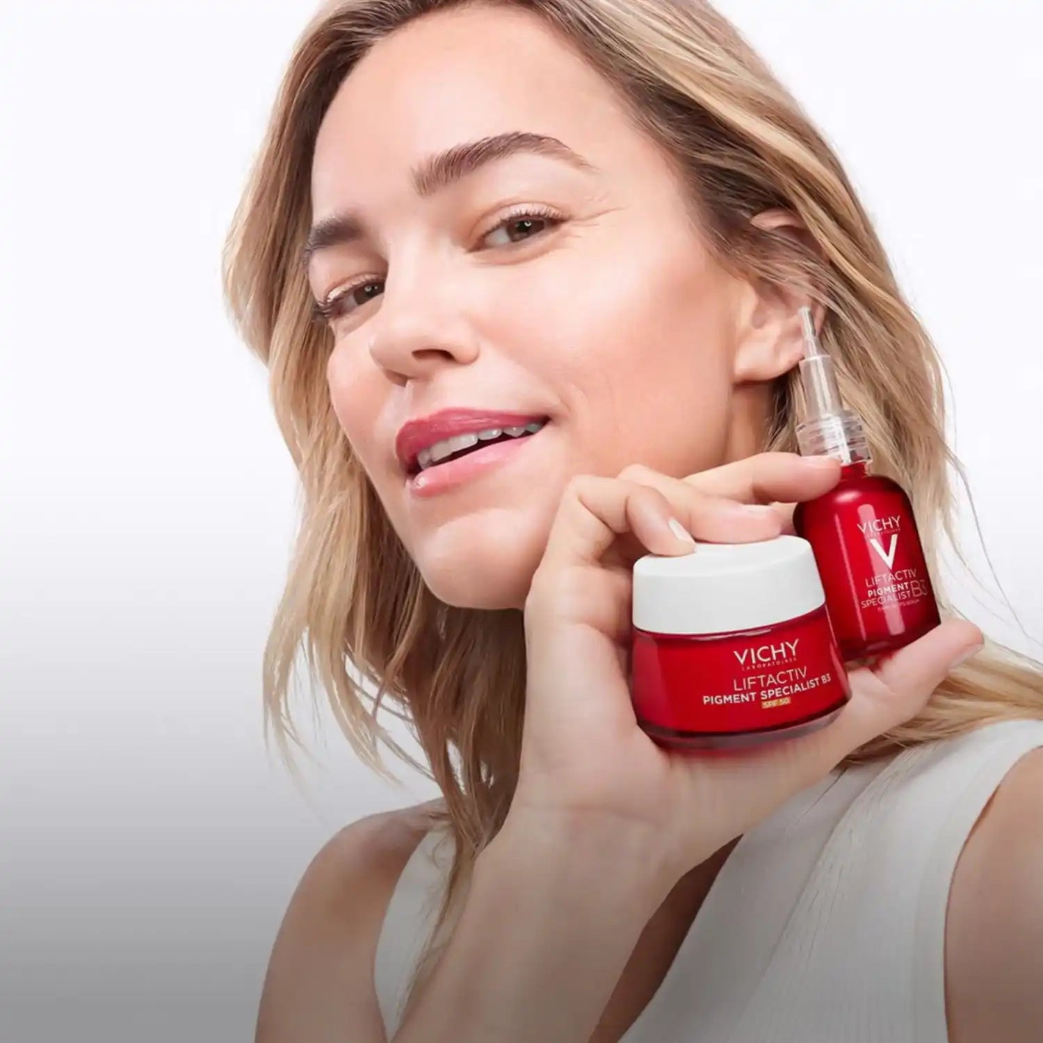 A woman holding two red Vichy skincare products.
