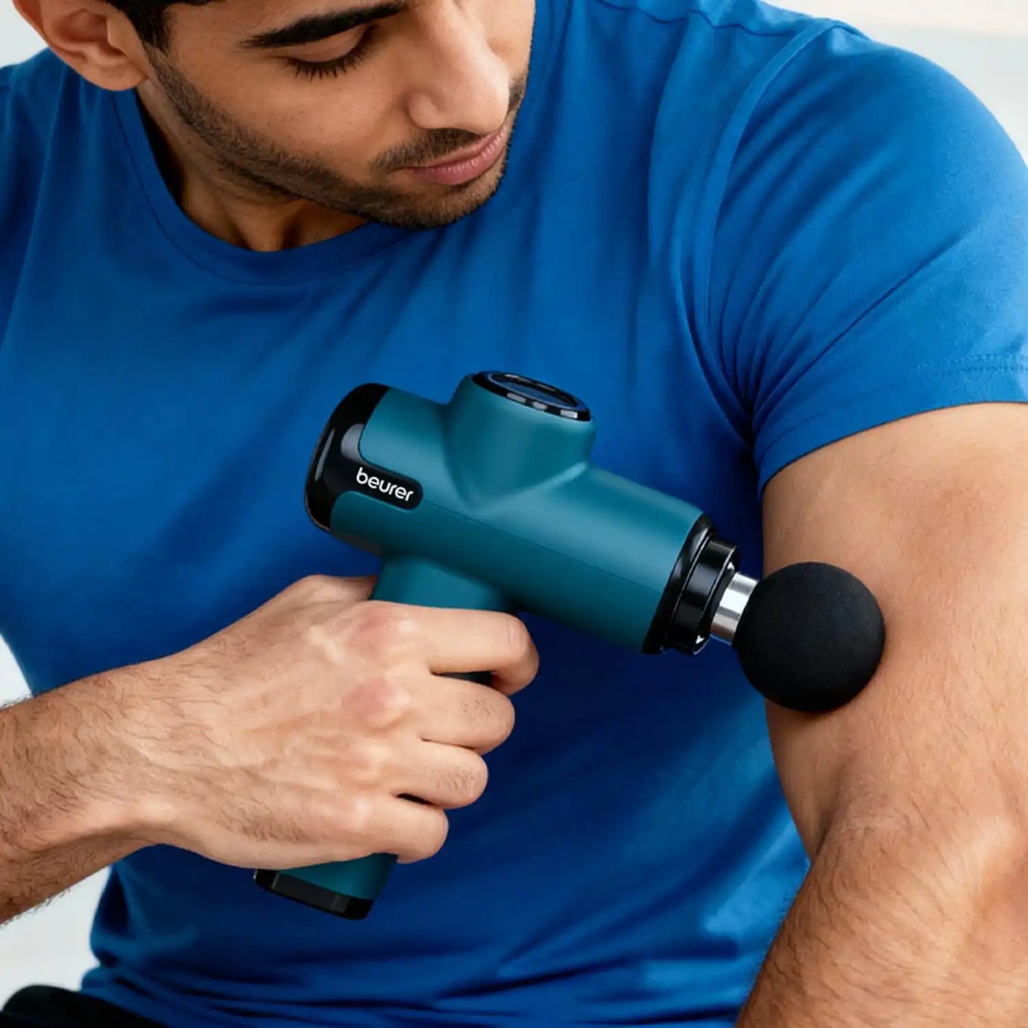 A teal Beurer percussive massage gun with a spherical black attachment.