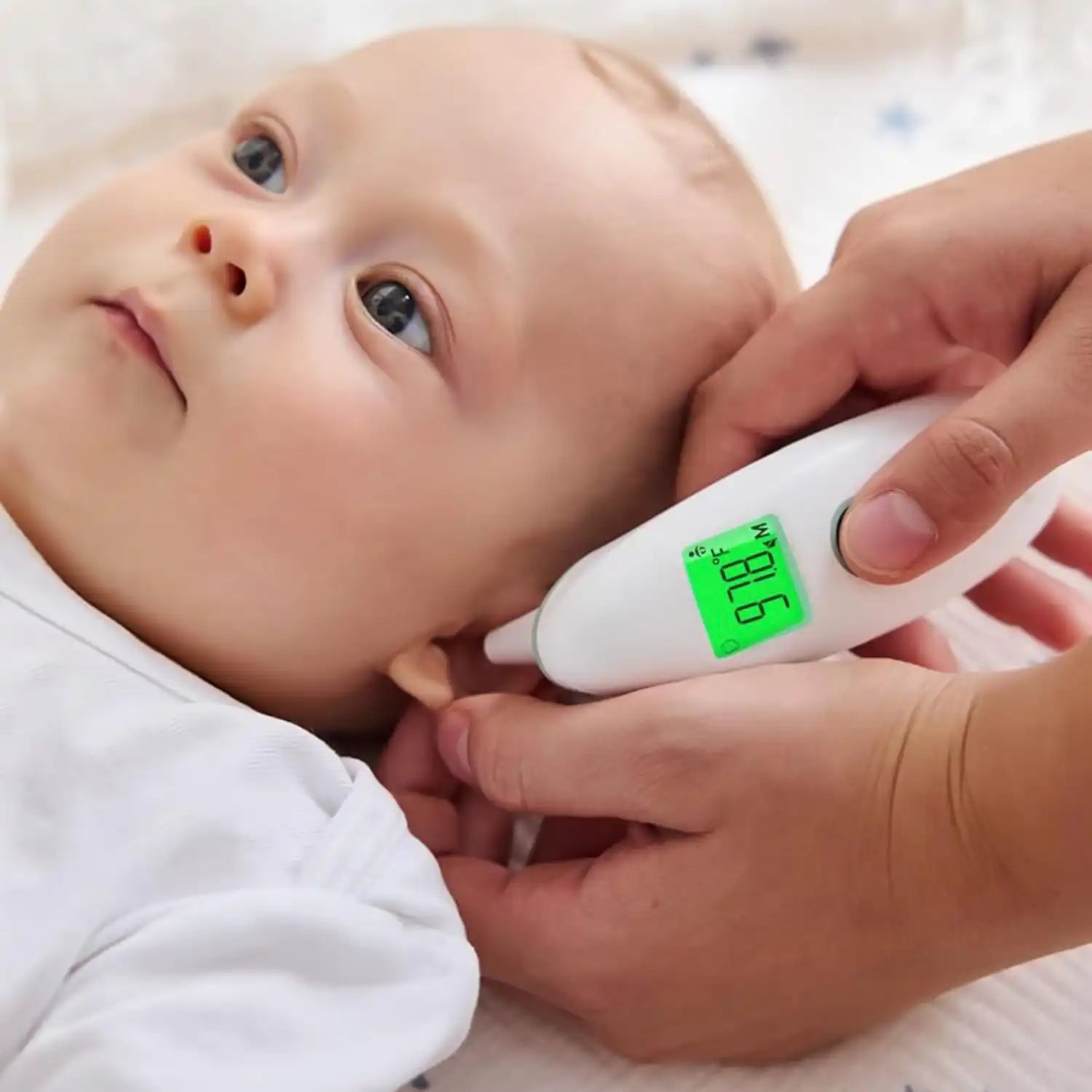 A person measuring a baby’s ear temperature with a digital thermometer displaying 97.8°F.