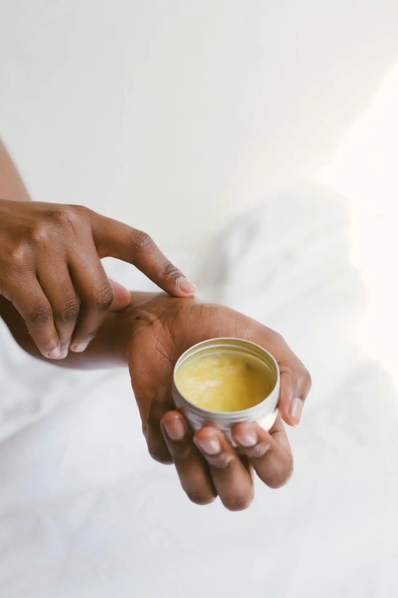 Hand applying yellow balm from metal tin.