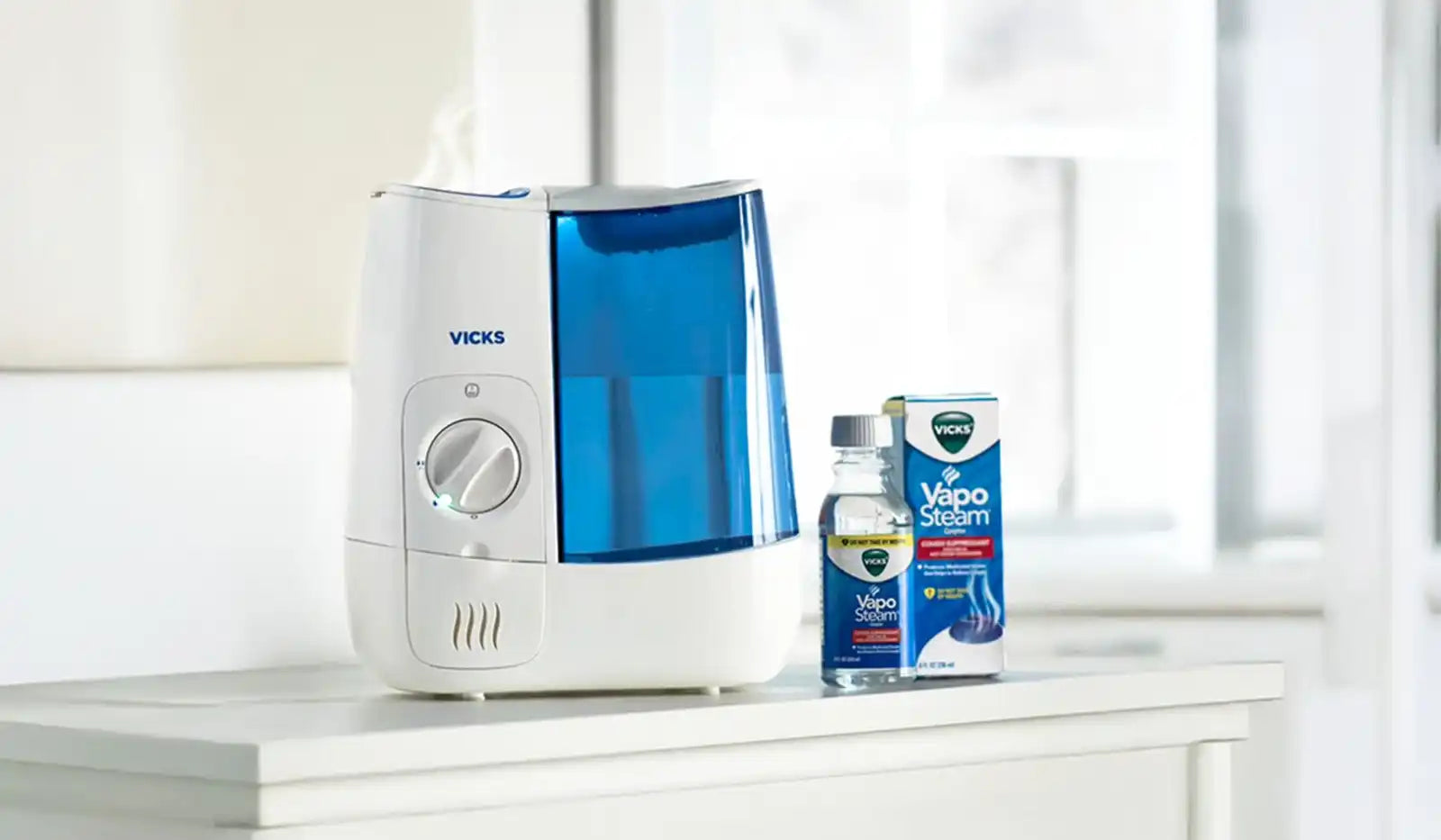 A white and blue Vicks humidifier with a bottle and box of VapoSteam.