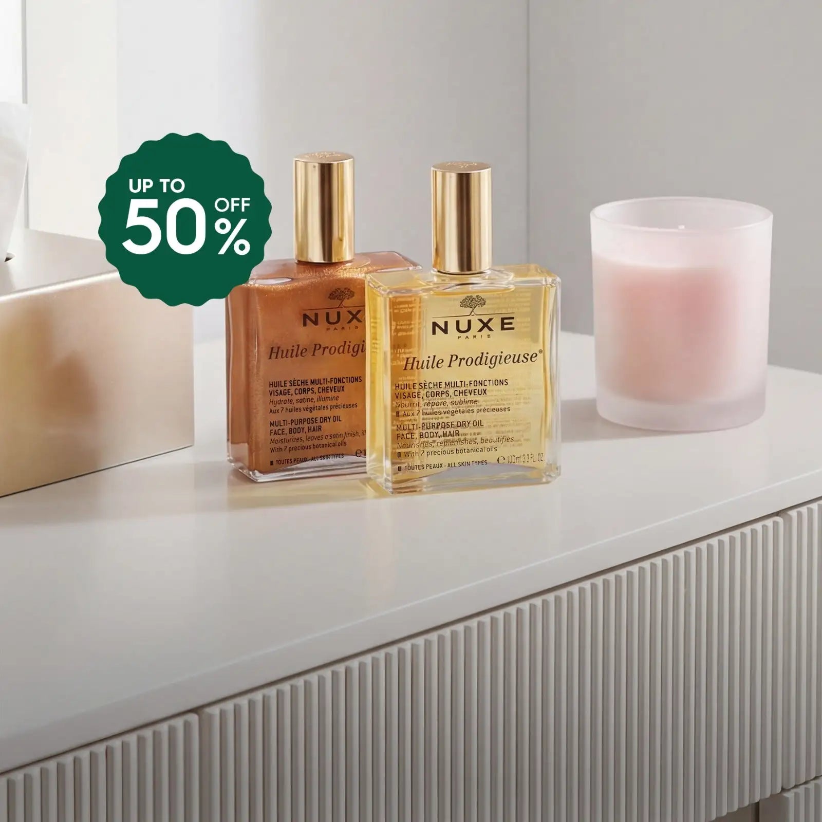 Two transparent glass bottles of nuxe huile prodigieuse multi-purpose dry oil, one amber and one golden-yellow, with gold caps.