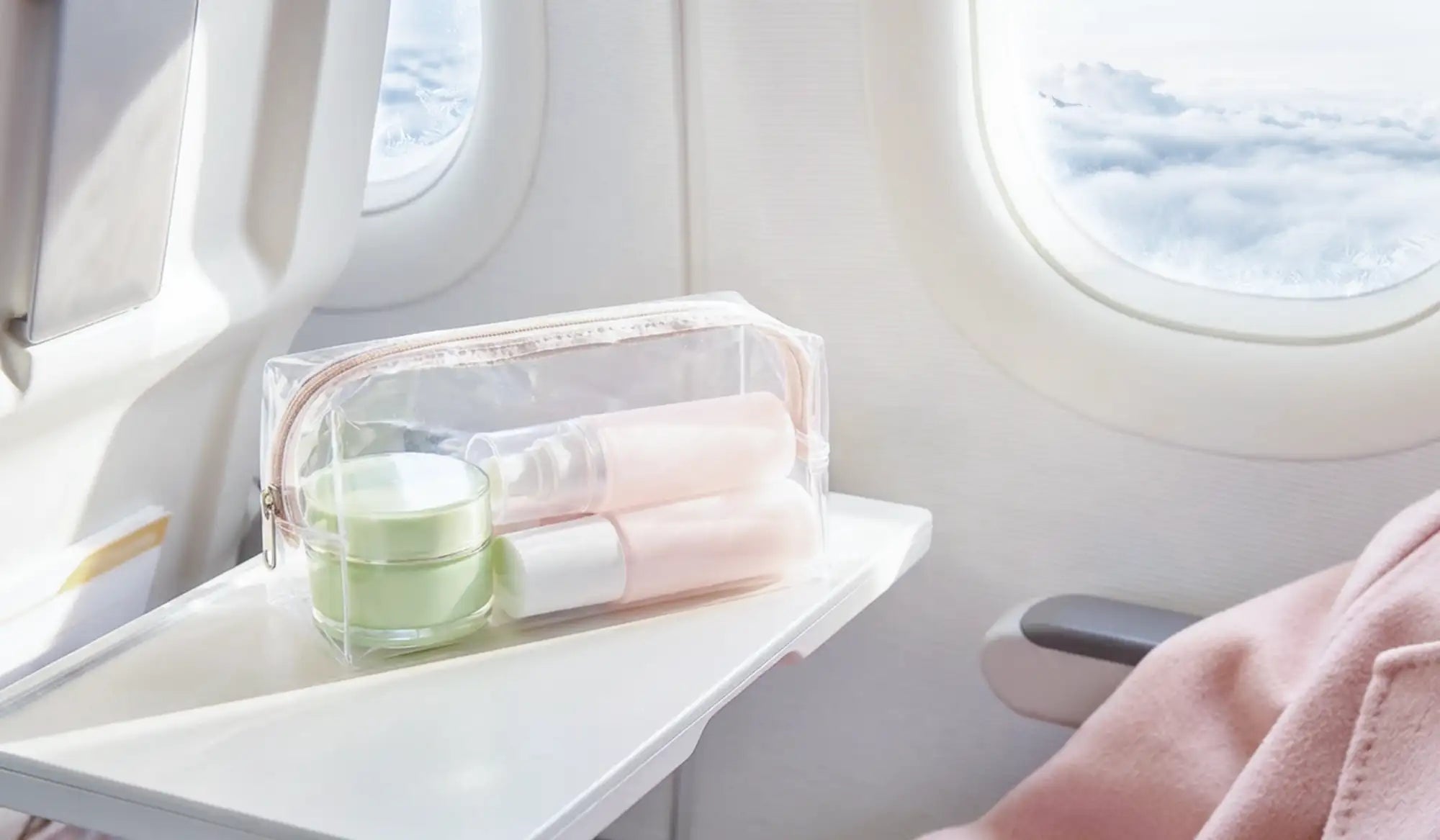 Clear plastic travel toiletry bag with rose gold zipper, holding pink and green skincare items.